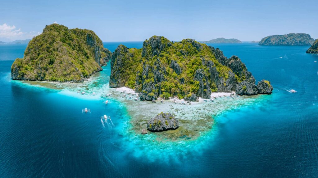 Aerial view of a small limestone island ringed by turquoise shallows near El Nido.