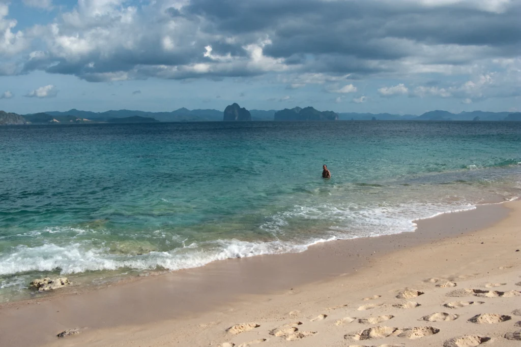 A white-sand beach on El Nido Bay, Palawan, with limestone cliffs behind it.