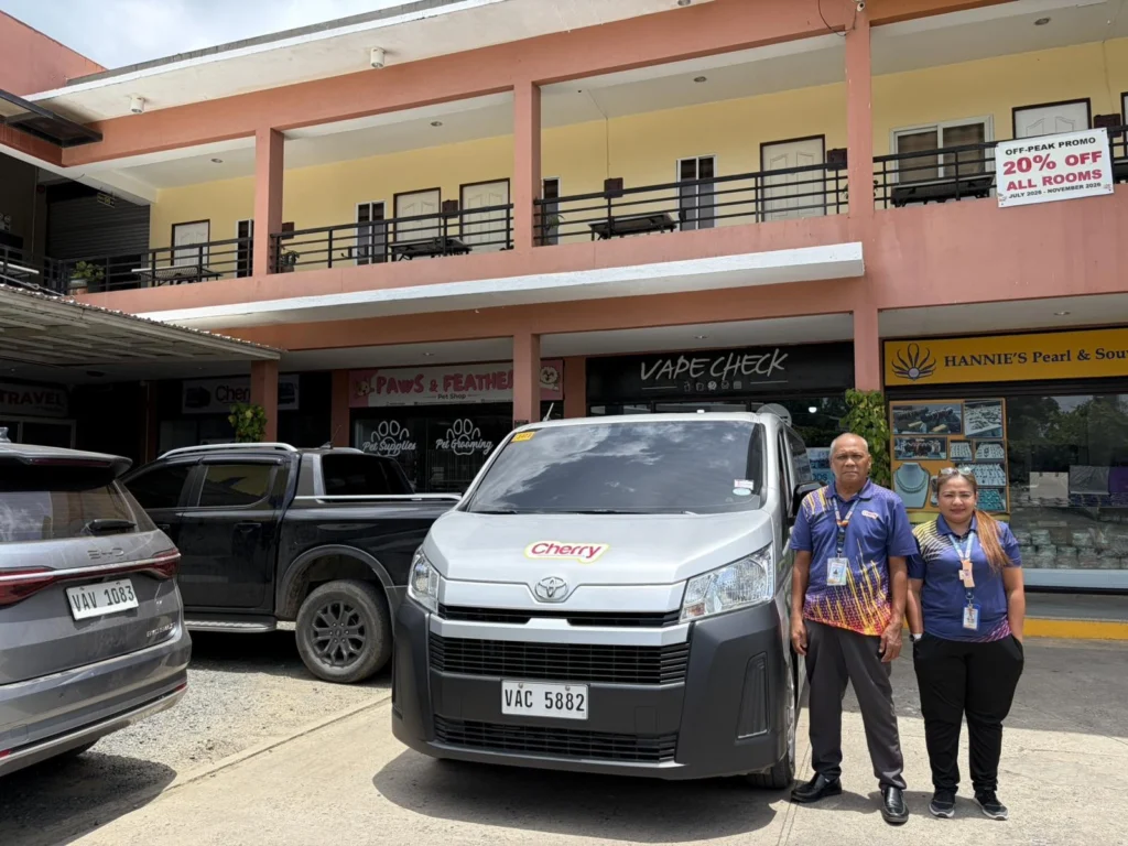 Two Cherry Bus staff in uniform standing beside a Cherry transfer van outside the Puerto Princesa ticket office.